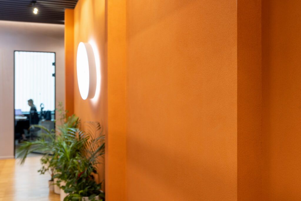 Orange matt textured wall in raking light with a round wall lamp